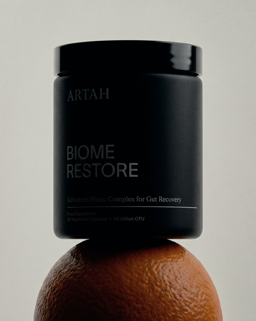 Matte black Biome Restore supplement jar balanced on fresh orange for Artah branding design by Two Times Elliott