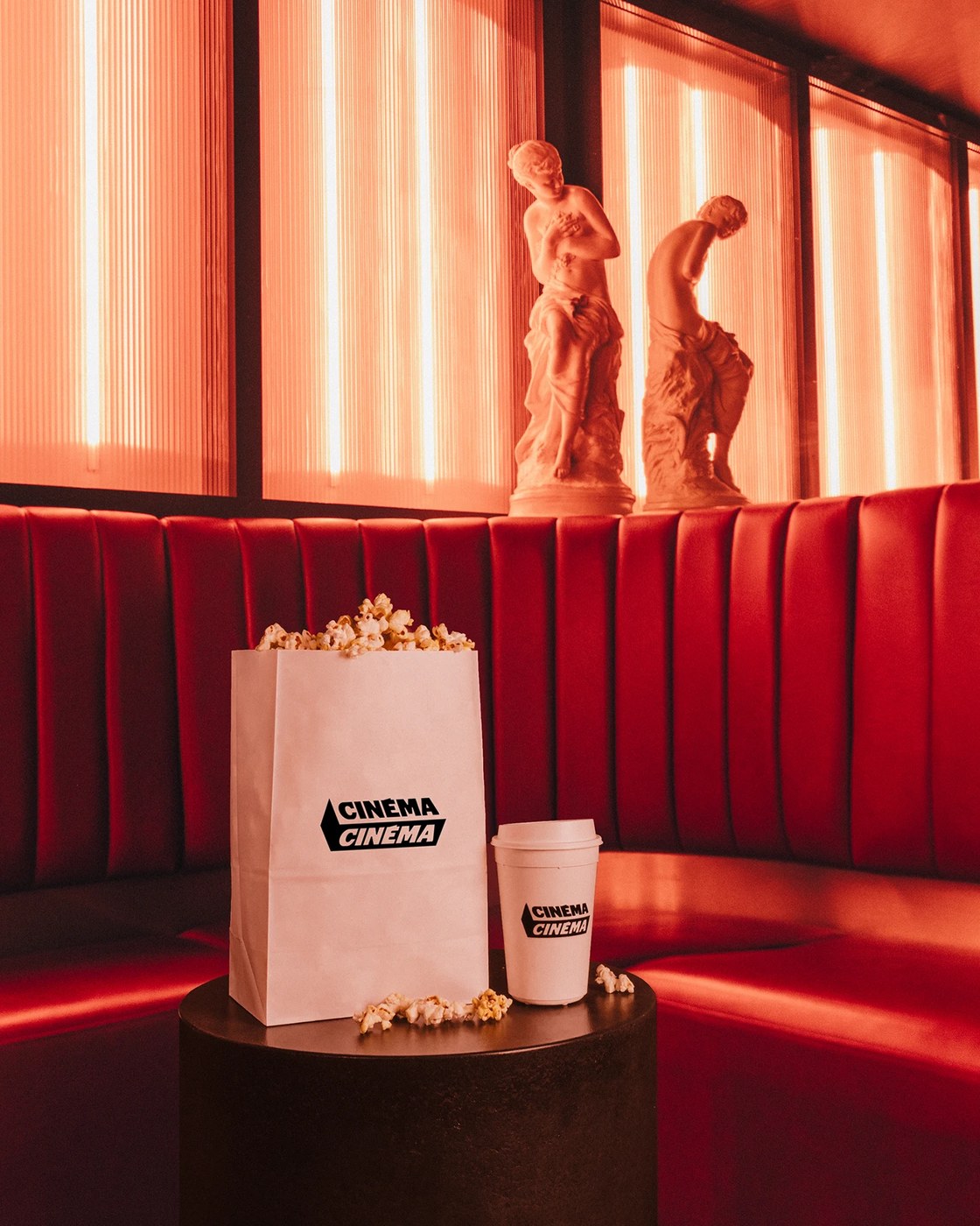 Cinéma Cinéma popcorn bag and coffee cup on concessions table against red banquette by Deux Huit Huit