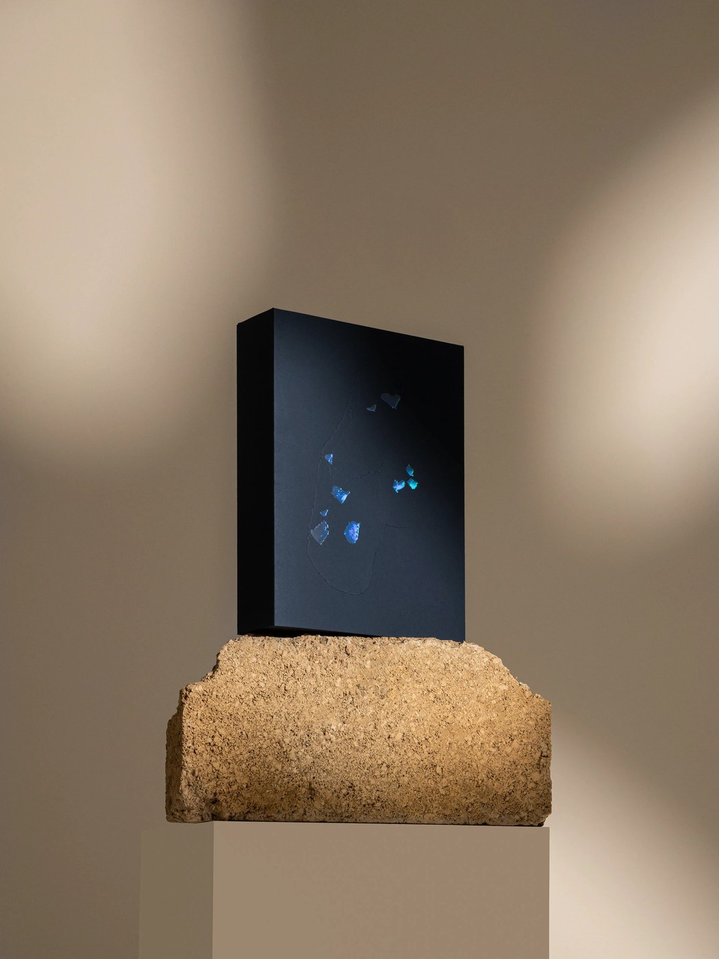 Sculptural black presentation book on rough stone plinth with iridescent foil insets — branding by Two Times Elliott