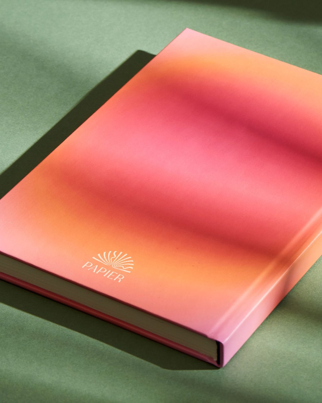 Gold foil stamped sunburst logo on hardcover notebook in Papier brand identity