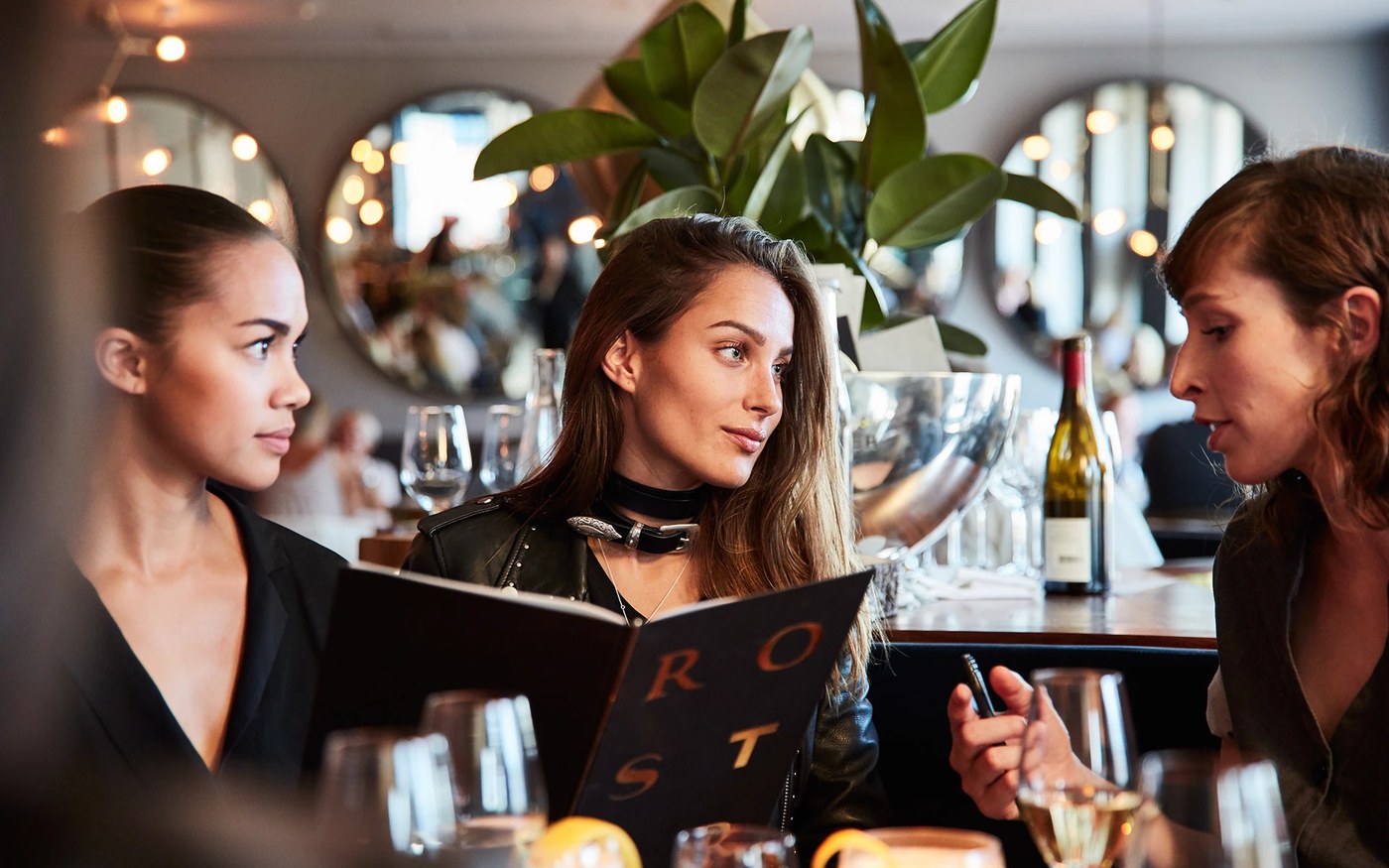 Restaurant patrons holding gold foil embossed Roster dining menu showcasing bespoke typography in branding design by BOND