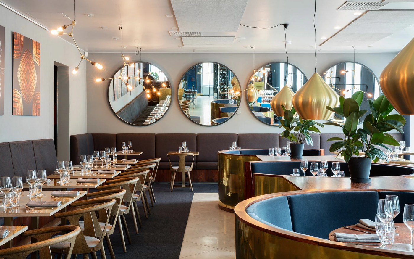 Interior dining room featuring circular wall mirrors, brass teardrop pendants, and curved banquette booths in branding design by BOND