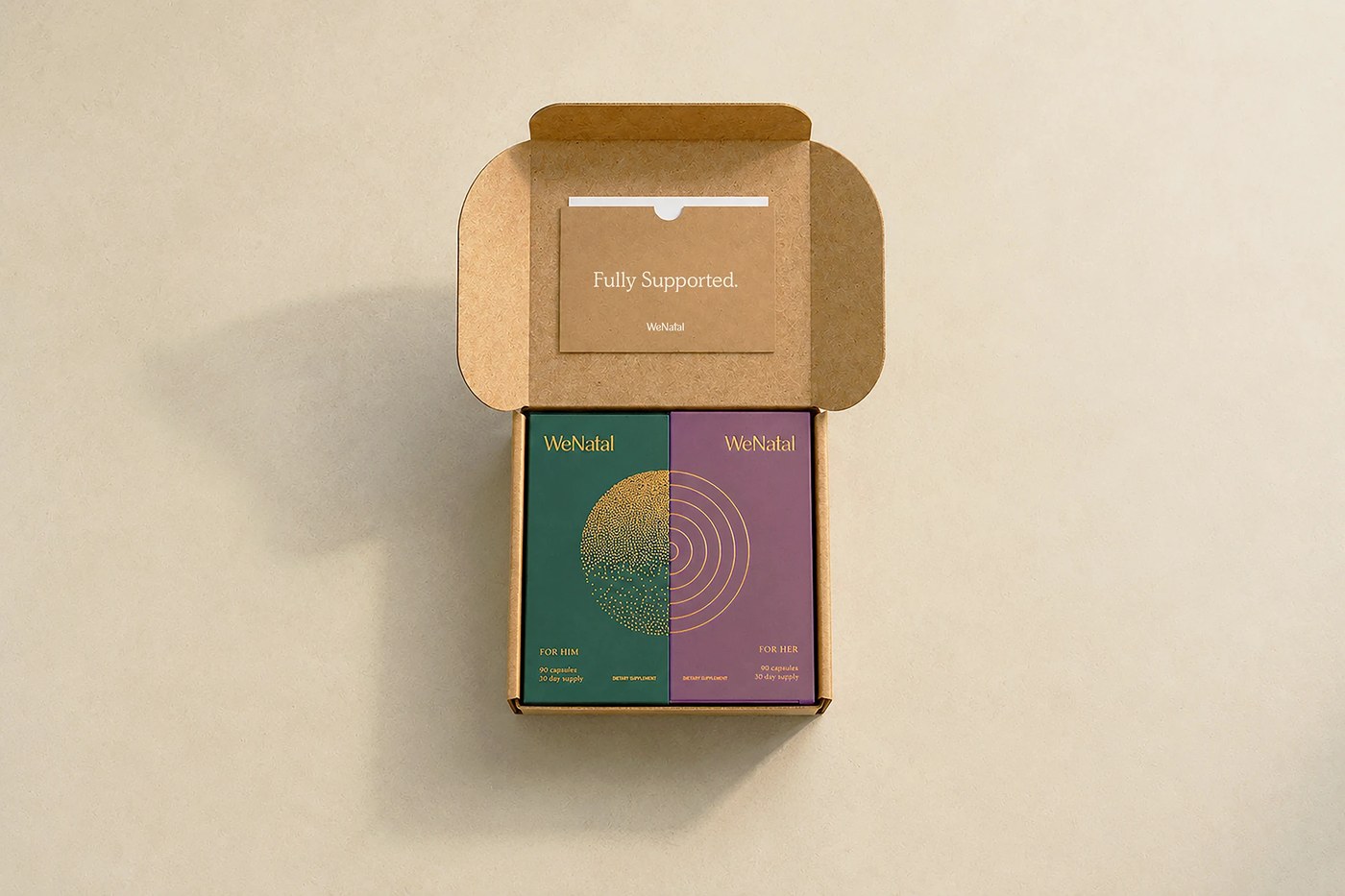 Top-down unboxing view of kraft box holding For Him and For Her supplement cartons with gold foil circle graphics and welcome envelope