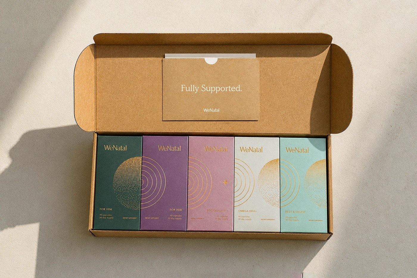 Unboxing setup box holding five WeNatal supplement cartons with gold foil geometric line art across diverse colorways