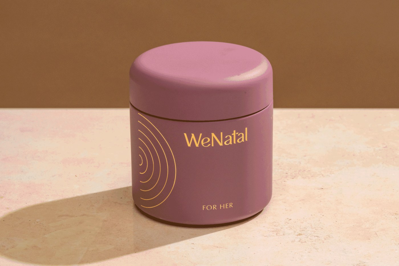 Rotating custom cylindrical mauve supplement jar featuring gold foil WeNatal wordmark and concentric ring graphics in packaging design